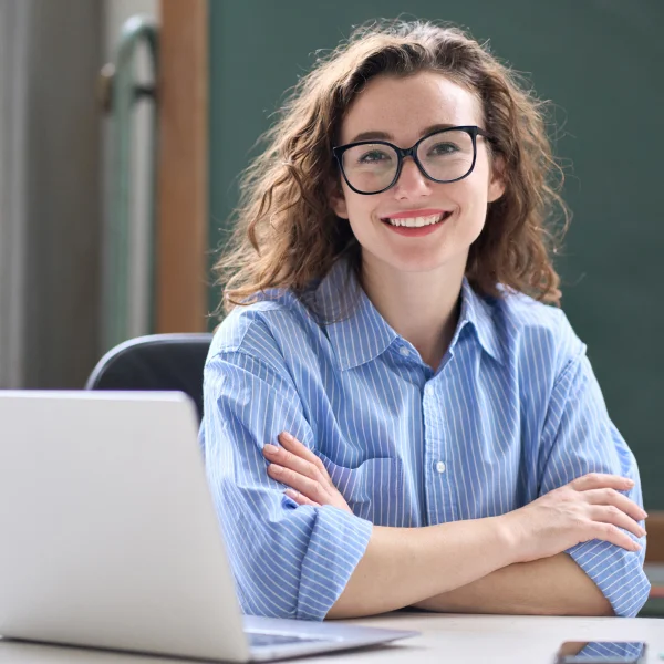 Une femme portant des lunettes est assise à un bureau avec un ordinateur portable devant elle.