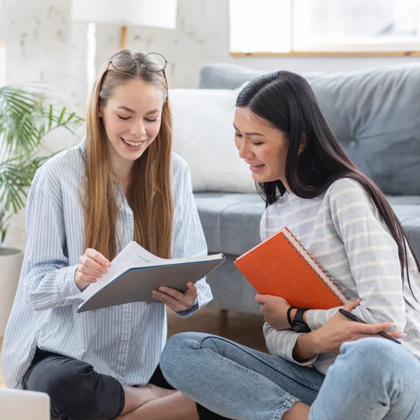 Deux jeunes femmes assises par terre, plongées dans la lecture et la discussion.