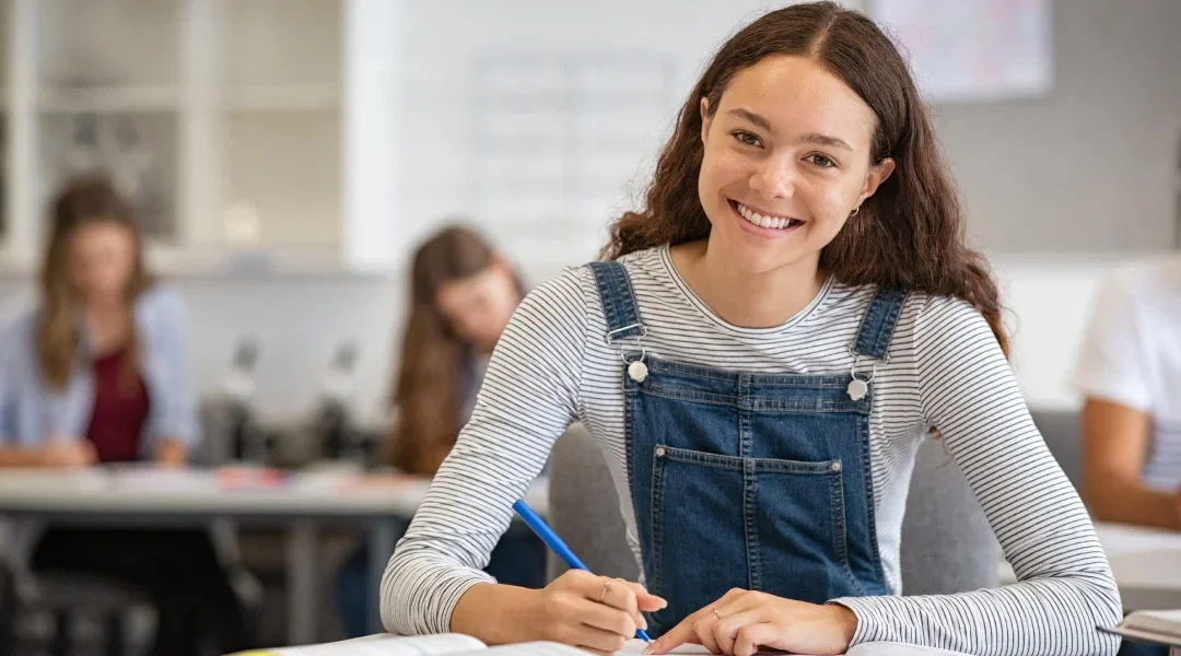 Une jeune fille, le sourire aux lèvres, prend des notes dans son carnet.