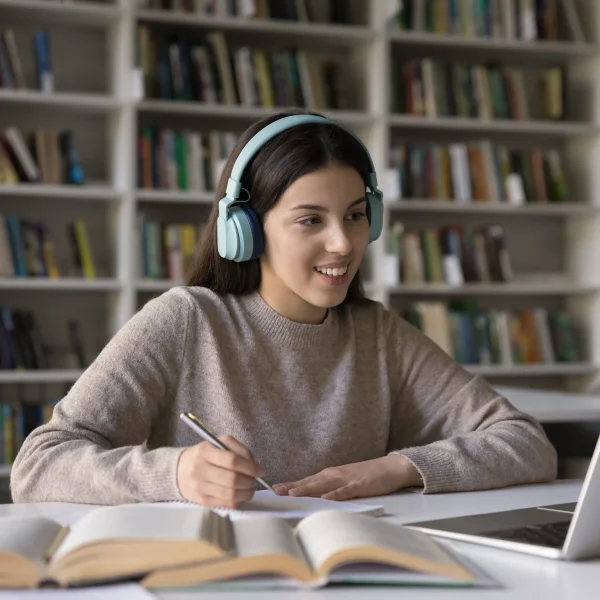 Une femme écoute de la musique avec des écouteurs, assise à une table avec son ordinateur portable.